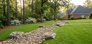 A professionally designed dry creek bed with river rocks and boulders on a sloped Atlanta residential lawn, used as an engineered solution for drainage and erosion control.